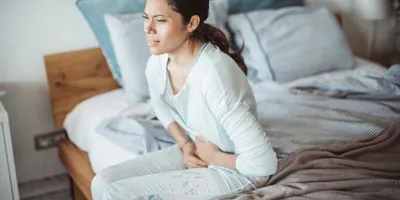 Žena s bolestí břicha sedící na posteli