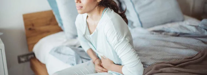 Žena s bolestí břicha sedící na posteli