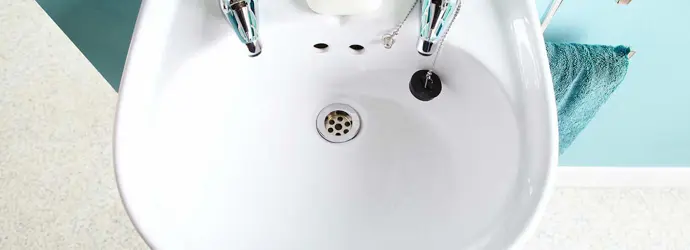 Horní pohled na umyvadlo se dvěma kohoutky a kostkou mýdla před tyrkysovými dlaždicemi