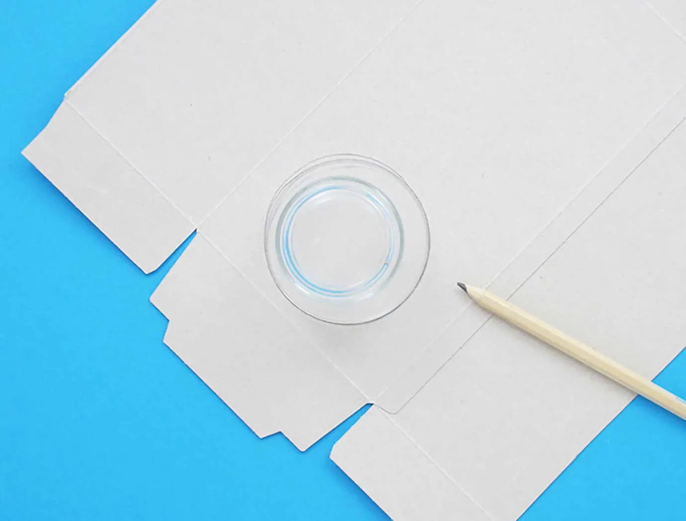 Otvorena i izravnana kutija maramica na plavoj površini s  malom čašom i olovkom.