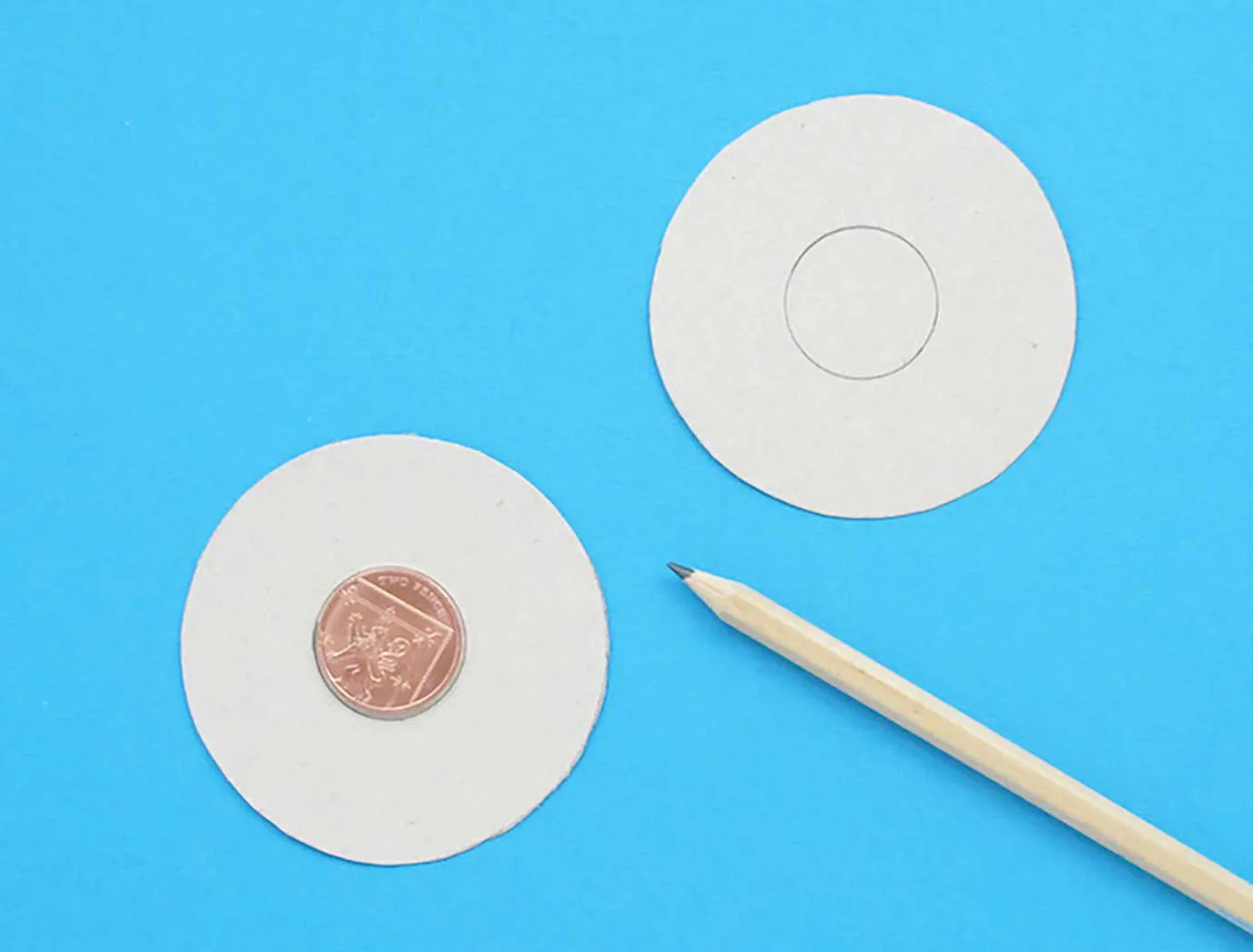 Dva kartonska izrezana kruga na plavoj površini s novčićem u sredini i olovkom sa strane.