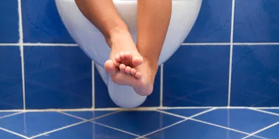 Dětské nohy visící z bílé závěsné toalety