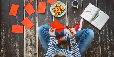 Egy nő Valentin-napi kártyákat ír házi készítésű Valentin-napi ajándékokkal, a földön ülve