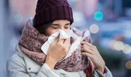 Nő bebugyolálva vastag téli ruházatba arcüreggyulladás tüneteivel, egy zsebkendőbe tüsszögve