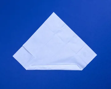 Fehér zsebkendő kiterítve, átlós helyzetben, az alsó egyharmada felhajtva, kék asztalon.