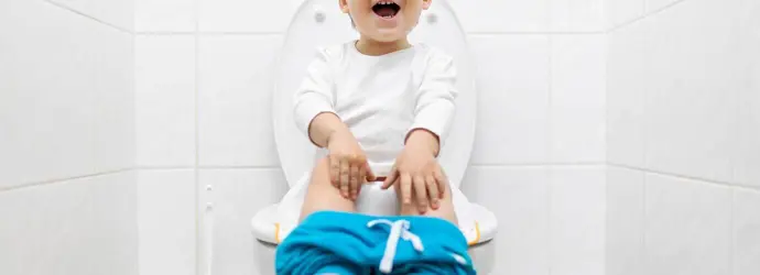 Ein kleines Kind sitzt mit heruntergelassener blauer Hose auf einer Toilette
