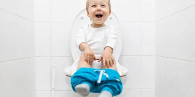 Ein kleines Kind sitzt mit heruntergelassener blauer Hose auf einer Toilette