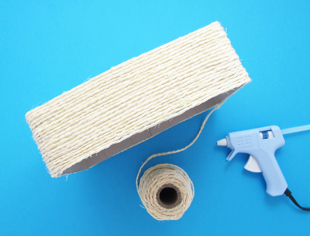 Egy zsinórral bevont kartondoboz ragasztópisztollyal és zsinórtekercssel, kék háttér előtt.