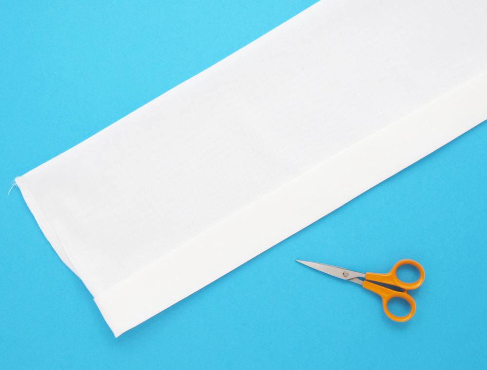 Hosszú fehér textilcsík narancssárga ollóval, kék háttér előtt.