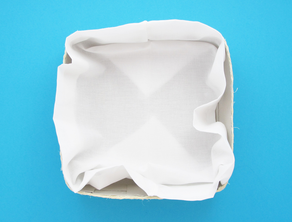 Egy fehér anyaggal kibélelt kartondoboz, kék háttér előtt.