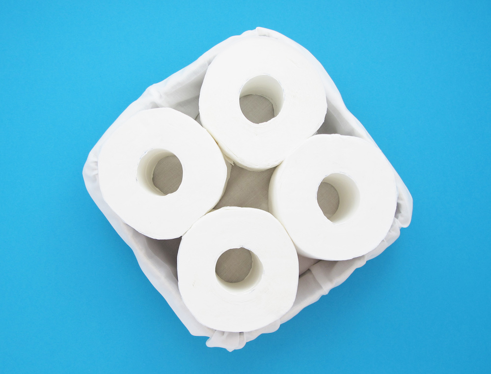 Egy fehér textillel bélelt doboz négy guriga toalettpapírral, kék háttér előtt.