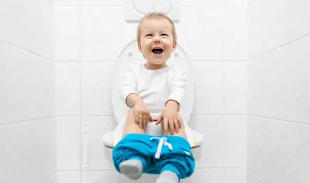 Dijete sjedi na WC-u u bijeloj kupaonici
