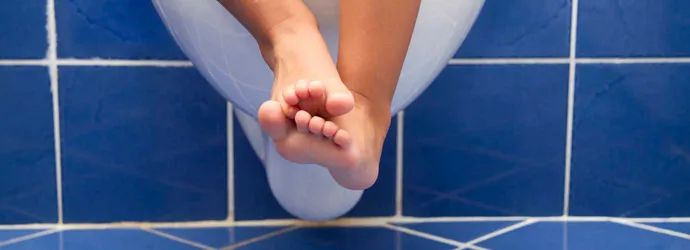 Τα πόδια ενός παιδιού που κρέμονται από τη λεκάνη της τουαλέτας