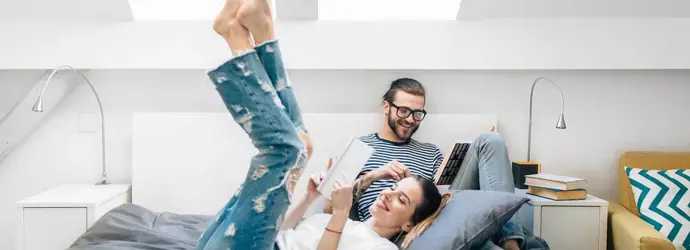 Ένα νεαρό ζευγάρι κάθεται σε ένα κρεβάτι και διαβάζει κάτω από δύο φεγγίτες