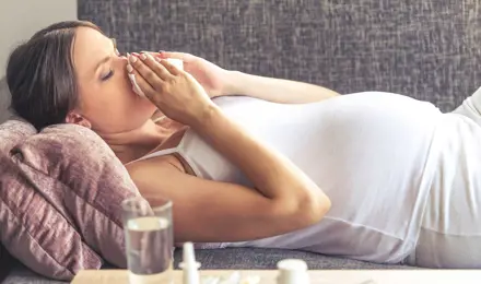 Молода вагітна жінка лежить із застудою на дивані.