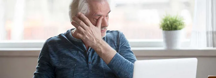 У літнього чоловіка, який сидить за комп'ютером, свербить одне око
