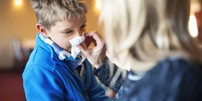 Egy édesanya náthás vagy influenzás kisfia orrához tart egy zsebkendőt, hogy segítsen neki az orrfújásban.