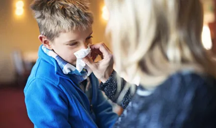 Egy édesanya náthás vagy influenzás kisfia orrához tart egy zsebkendőt, hogy segítsen neki az orrfújásban.
