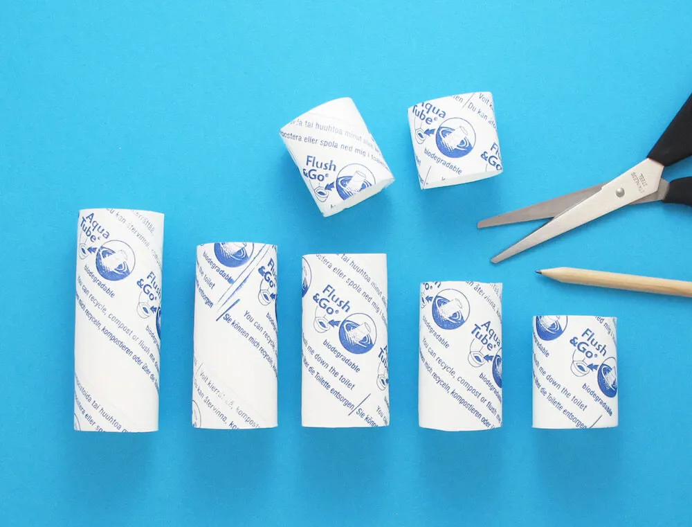 Пет картонени ролки от хартия в различни рамери, поставени до  ножица и молив.