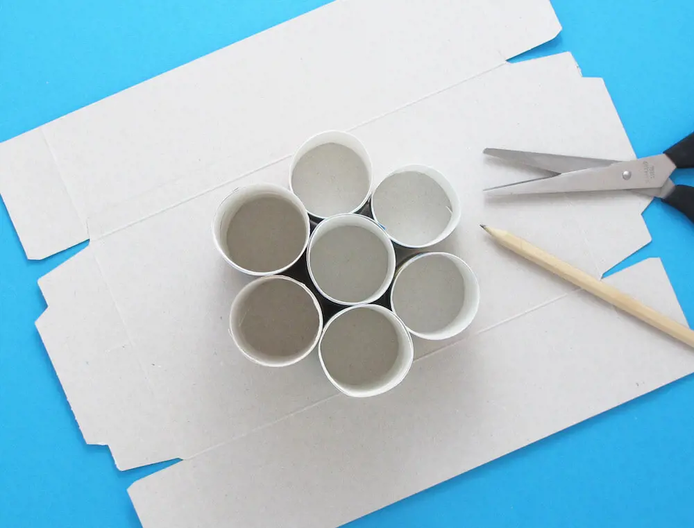 Картонени ролки, завити в цветна хартия, залепени една за друга, върху разгърната кутия от кърпички.