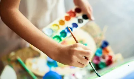 Ein Kind malt mit einem Pinsel auf einer Leinwand und hält eine Farbpalette in den Händen
