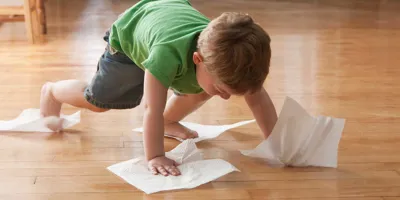 Copil care curăță podeaua cu prosoape de hârtie