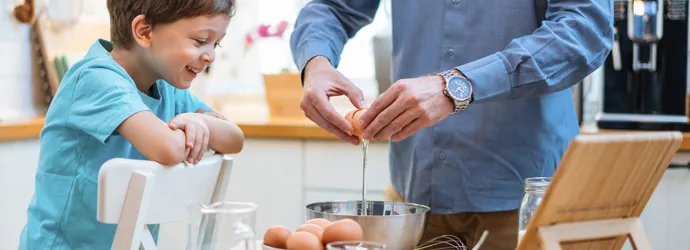 Egy férfi és egy gyerek vidáman törik fel a tojást egy keverőtálba.