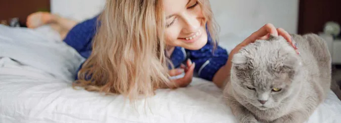 Женщина лежит на кровати, поглаживая кошку, и не представляет симптомы аллергии на кошек
