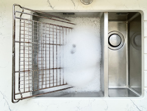 Schmutzige Backgitter und Ofenroste weichen in einem Waschbecken mit Seifenwasser ein.