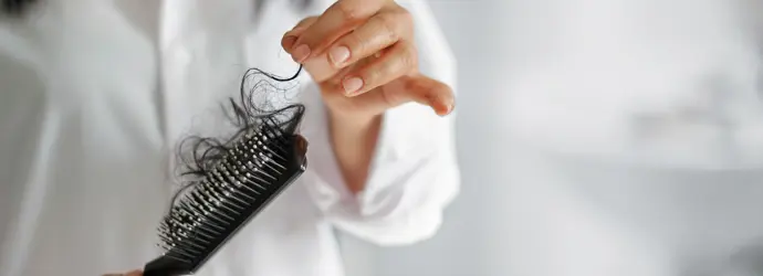 Eine Frau in einem weißen Hemd zieht vorsichtig lange, dunkle Haare aus einer schwarzen Haarbürste.