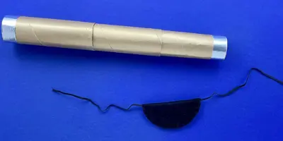 Ein goldenes, selbstgemachtes Fernrohr aus Pappe neben einer schwarzen DIY Augenklappe auf blauem Hintergrund.