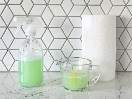 Eine Sprühflasche und ein gläserner Messbecher mit Zitronenreiniger und einer Rolle Küchentücher.