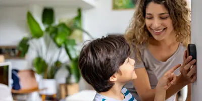 Eine lockige Mutter zeigt einem lächelnden Jungen ihr Thermostat.