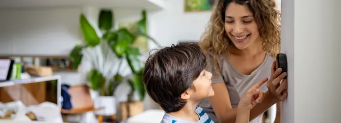 Eine lockige Mutter zeigt einem lächelnden Jungen ihr Thermostat.