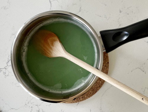 Ein Topf auf einem Untersetzer aus Kork mit den Zitronenreiniger und einem hölzernen Kochlöffel.