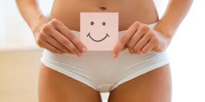 Eine Frau in Unterwäsche hält einen Zettel mit Smiley an ihren Bauch.