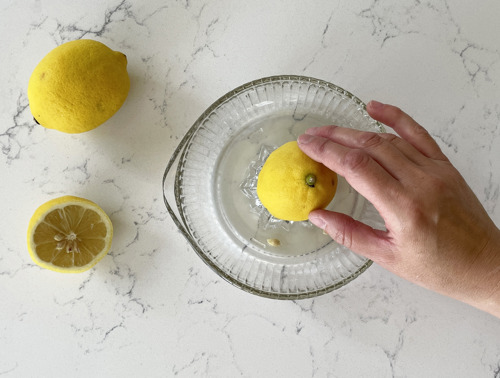 Eine Zitrone wird mit Hilfe einer gläsernen Zitronenpresse entsaftet.