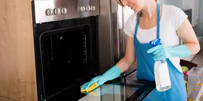 Eine Frau in einer dunkelblauen Schürze reinigt mit einem gelben Tuch den Backofen.