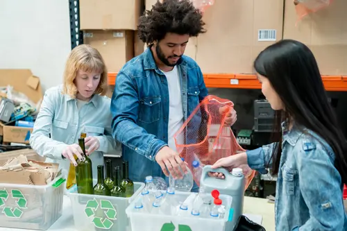 Τρία άτομα ταξινομούν το χαρτόνι, το γυαλί και το πλαστικό σε ξεχωριστά δοχεία.