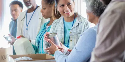 Жінка передає іншій жінці невиразну бляшанку з їжею.