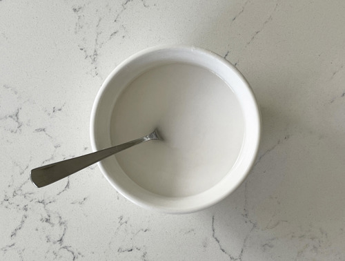 Eine weiße Schüssel mit der Backpulver-Essig-Paste und einem silbernen Löffel.