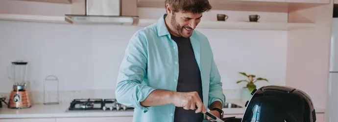 Ein Mann mit braunen Haaren und Bart reinigt eine Heißluftfritteuse in einer Küche.