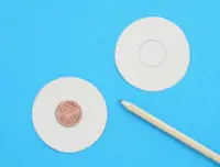 Dva kartonska izrezana kruga položena na plavu površinu sa novčićem u sredini jednog i olovkom sa strane.