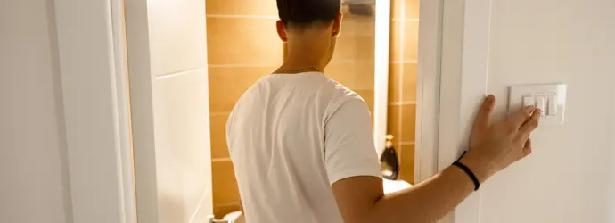 Muž v bílé košili zhasíná světla v místnosti s kachličkami.