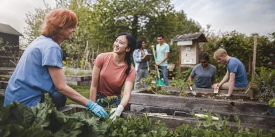 Eine Gruppe von Menschen jeder Altersgruppe arbeiten freudig gemeinsam in einem Community Garten und pflanzen Obst und Gemüse an.